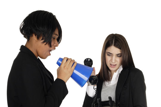 One Woman Yells Through Megaphone Into A Phone Held By Cringing Second Woman.