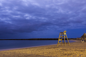 Fototapeta premium High wooden lifesaver chair on tropical sandy deserted beach night shoot