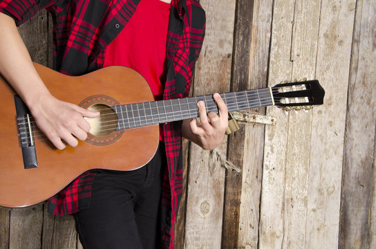 young man no face, playing guitar in plaid shirt next to wooden barn door