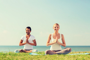Fototapeta premium smiling couple making yoga exercises outdoors