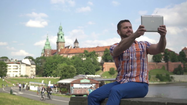 Man takes a selfie, sitting on the wall.
