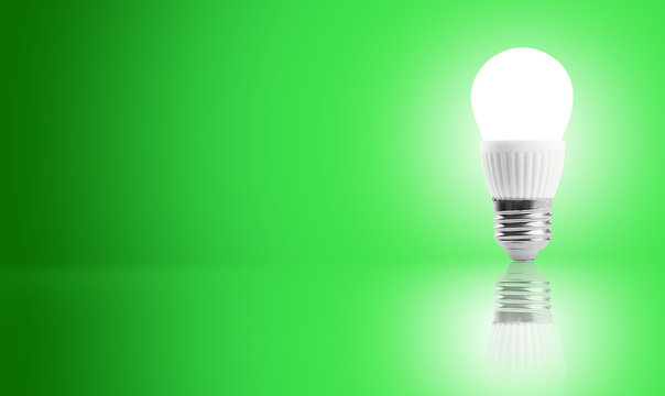 Glowing LED Energy Saving Bulb On A Green Background.