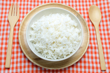 bowl full of rice in plate and spoon on wood