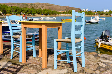 Fototapeta premium Traditional Greek taverna on the seafront on the beach - bright chairs and table, Pollonia village, Milos island, Cyclades, Greece.