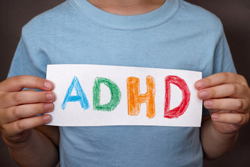 Young boy holds ADHD text written on sheet of paper