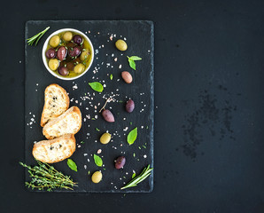 Mediterranean olives with herbs and ciabatta slices on black
