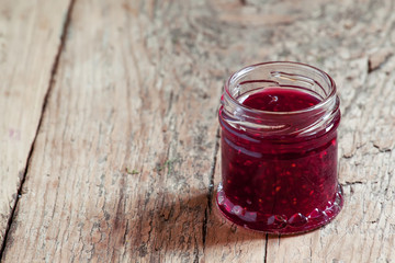 Raspberry jam with fresh raspberries and green leaves on the old