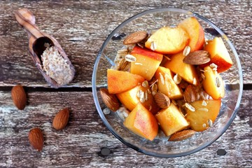 Nutritious overnight oats with fresh peaches and almonds, overhead view on a rustic wood background