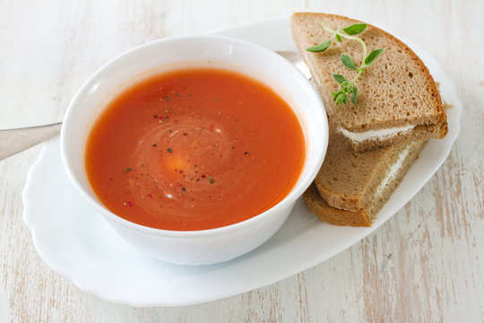 tomato soup in white bowl with sandwich on white background