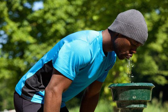 Young Black Man Drinking Water From A Water Fountain