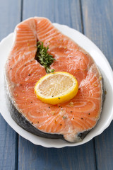 fresh salmon with lemon on white dish on blue wooden background