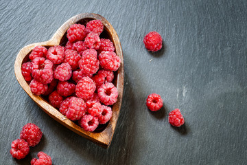 Fresh raspberries in a bowl in the shape of a heart on a dark ba