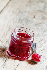 Raspberry jam in a jar and raspberries in a spoon on old wooden