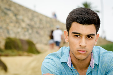 Close up of young handsome man, looking serious. People walking in background.