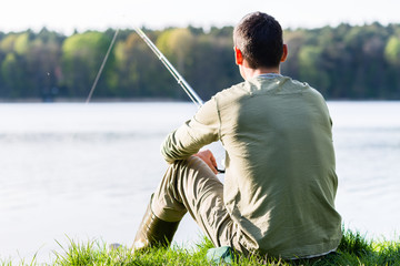 Angler beim Angeln am See sitzt im Gras