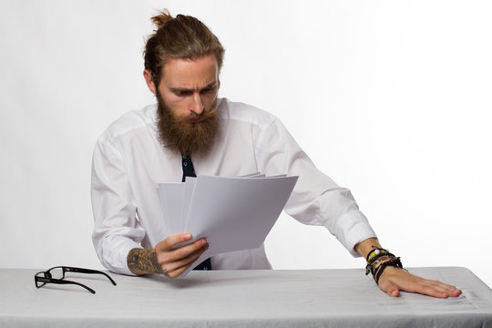 Handsome young businessman with beard and glasses thinking at the table on white background 