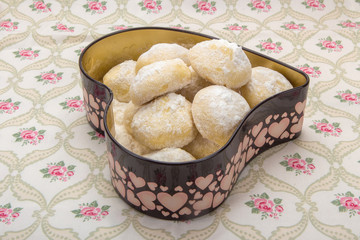 Small cookies in powdered sugar in a tin box in heart shape on cotton napkin with floral pattern