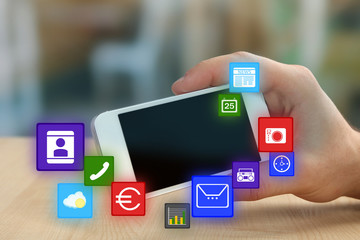 Smart-phone in hand and icons around on blurred color background