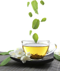 Mint leaves falling in cup of jasmine tea isolated on white