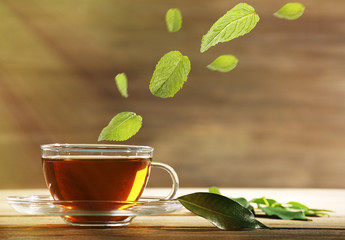 Mint leaves falling in cup of green tea on wooden background