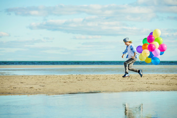 Happy boy plays with colored balloons on the beach