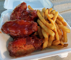 Take-out chicken wings in barbeque sauce and French fries for a picnic in the park.
