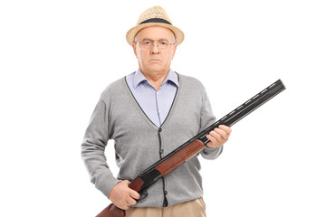 Serious senior gentleman holding a shotgun and looking at the ca