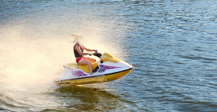 Adult having fun jumping a wave riding yellow and white Sea Doo jet ski in California Ocean