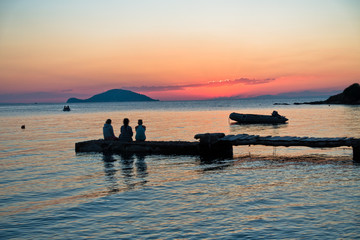 Naklejka na ściany i meble Girls sitting on a pier at sunset in Sithonia