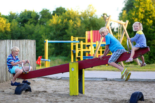 Happy kids enjoying active summer vacation. Group of happy children, blond cute toddler girl and two schoolboys, having fun outdoors swinging on playground in the park on a sunny day