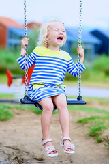Happy kid enjoying active summer vacation. Adorable little child, blond cute toddler girl, having fun outdoors swinging on playground in the park on a sunny day