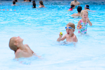 Happy family having fun in recreation swimming pool. Children enjoying day in waterpark during active summer holidays. Kids laughing and playing with waterguns. Selective focus on little girl.