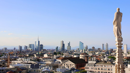 Panoramic view of Milan skyline from Duomo cathedral. Religious statue faces to the buildings of the financial district. The Alps mountains on the background.