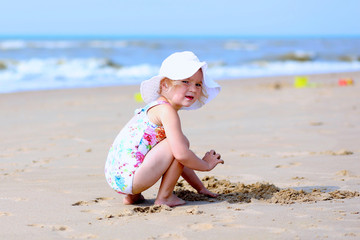 Cute active child wearing white hat playing on sandy beach. Happy little girl enjoying summer holidays on a sunny day. Family with young kids on vacation at the North Sea coast.