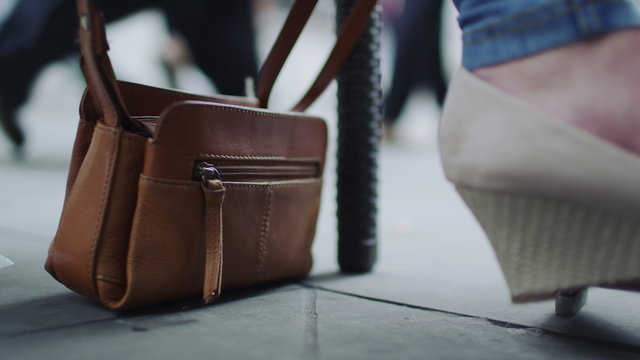 4K Close up of a woman's handbag on the floor as pedestrians walk by in the blurred background, crime concept, shot on RED EPIC