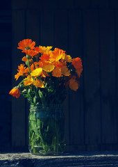 Yellow summer flowers in a glass jar on an old wooden surface. Bouquet from a marigold. Calendula flowers. Festive card.