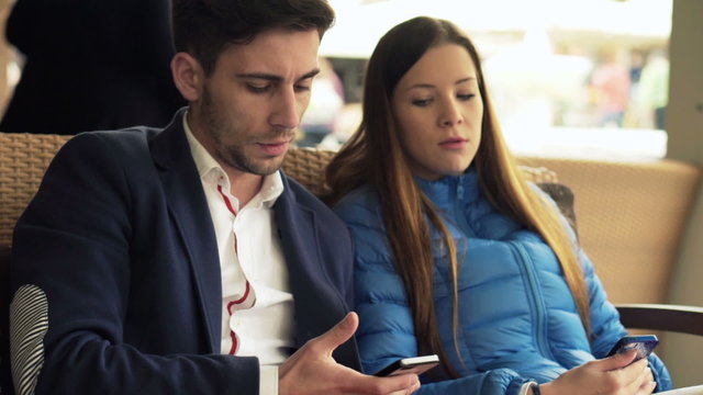 Young couple showing something to each other on smartphone in cafe in city
