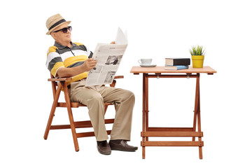 Senior sitting at a coffee table and reading a newspaper