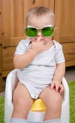 Funny baby boy with vintage green glasses on a white plastic potty  - 88477875