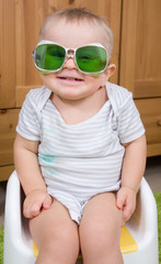 Funny baby boy with vintage green glasses sitting on a plastic child potty - obrazy, fototapety, plakaty