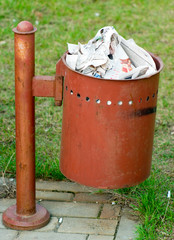 Rusty metal dustbin full of newspapers on a green grass background - 88478673