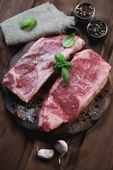 Fresh striploin steaks with seasonings, rustic wooden surface