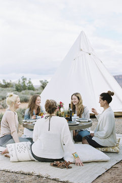 Group of women enjoying an outdoor meal by a teepee in the desert. 