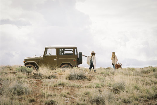 Two women by a jeep in open space, loading up for a road trip. 