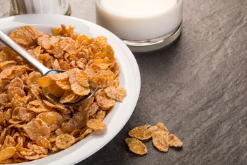 Corn Flakes auf einem Teller und Milch in einer Flasche auf einer schwarzen Granitplatte