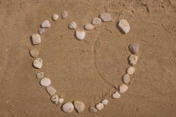 Fototapeta na wymiar Heart made with pebbles on the sand by kids
