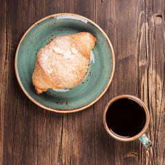 Fresh croissant and mug of black coffee on wooden table. Top view. Vintage style. Space for text