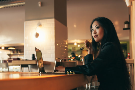 Elegant Asian Businesswoman Working with a Laptop in a Restauran