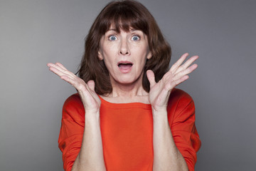 surprise and disappointment concept - beautiful 50s woman wearing a red sweater expressing surprise...