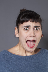 fear concept - portrait of terrified 20s woman with blue winter sweater screaming out,mouth wide open ,studio shot